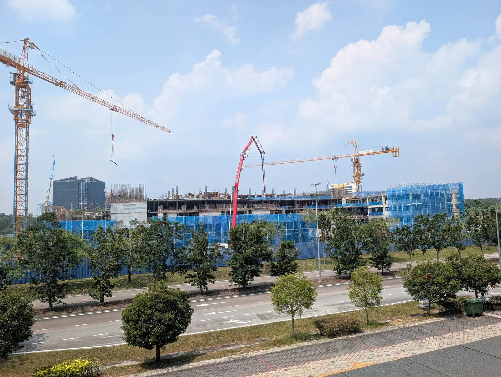 Tower A superstructure rising behind blue safety screens at the Bodaiju Residences site in Medini, with two tower cranes and a concrete pump boom working on the upper deck, August 2026
